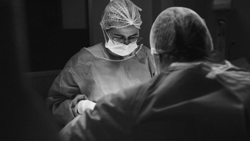 Two surgeons operate under focused lighting in a sterile environment.